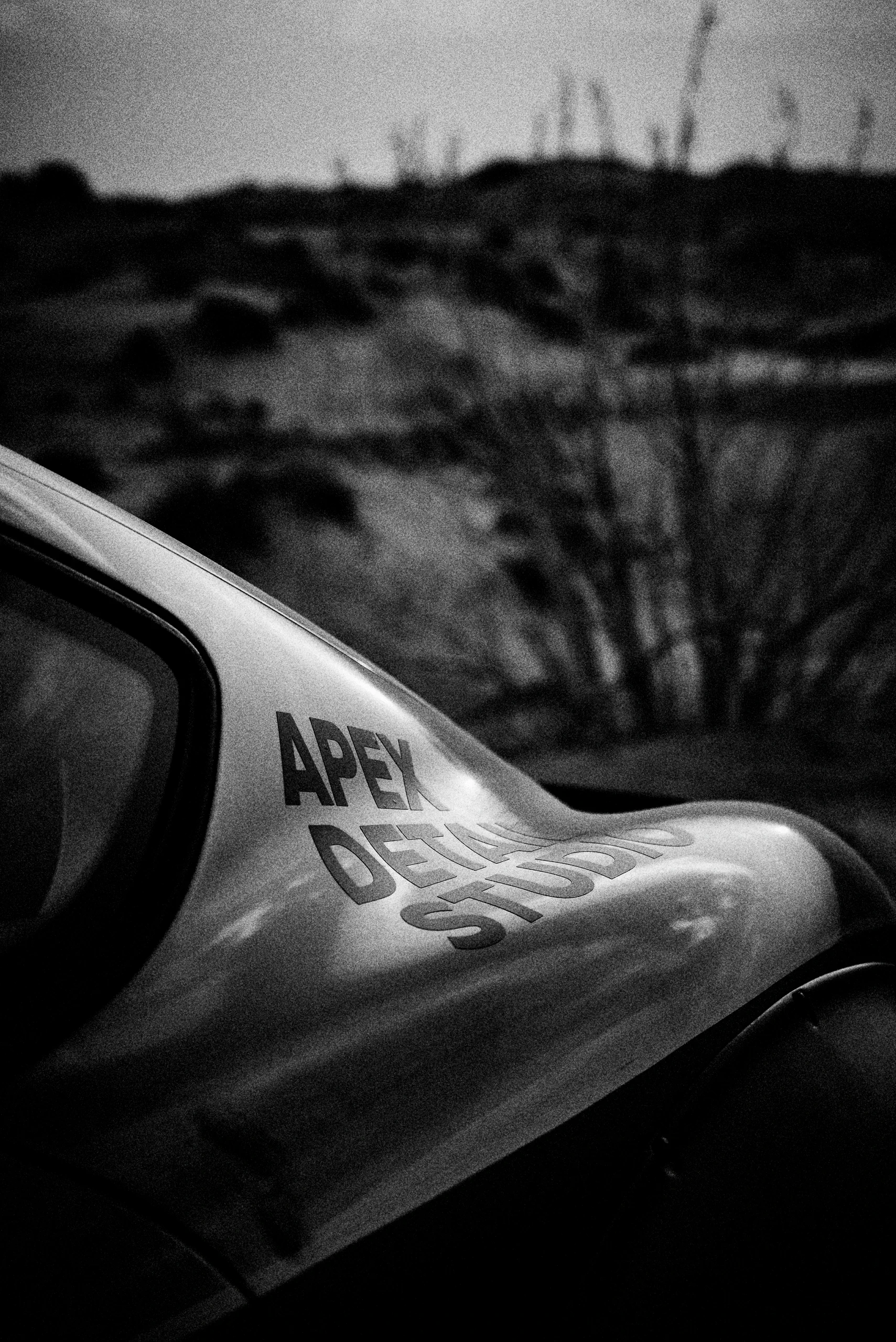 Grainy black-and-white panning photograph of an off-road Porsche Cayman driving along a desert road.