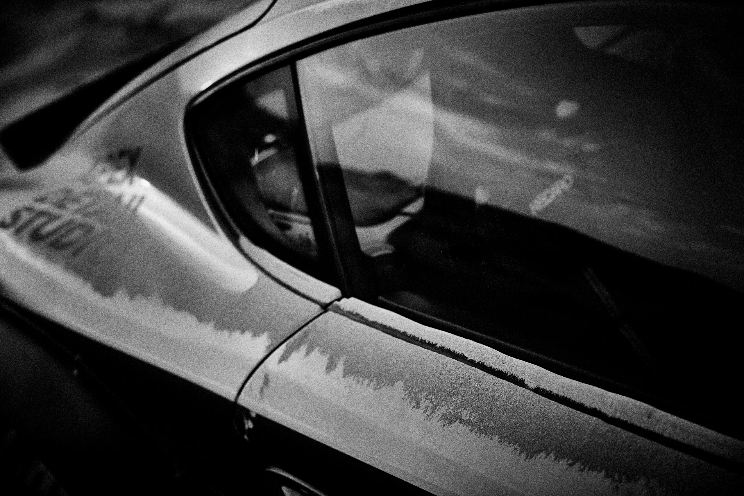 Grainy black-and-white panning photograph of an off-road Porsche Cayman driving along a desert road.