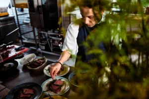 A chef cooking in the kitchen seen through garden foliage