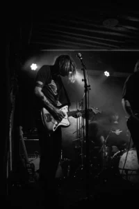 Black-and-white photograph of a SØWT guitarist leaning over an electric guitar during a concert in Cologne.