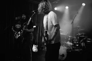 A member of SØWT performing at a microphone under stage lights at Bumann & Sohn in Cologne.