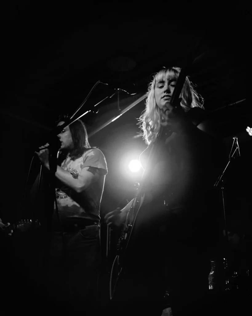 Black-and-white portrait of a REAL FARMER band member singing into a microphone under stage lights.