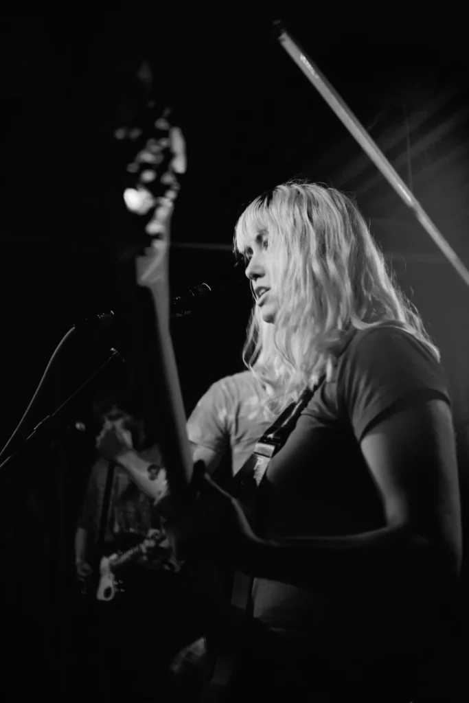 Black-and-white close-up of the REAL FARMER bassist performing onstage in Cologne.
