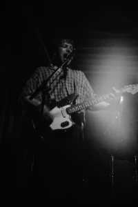 A REAL FARMER guitarist performing in backlight during a black-and-white concert photograph.