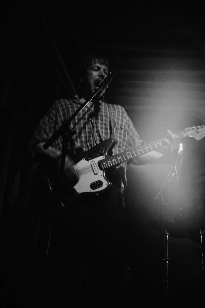 A REAL FARMER guitarist performing in backlight during a black-and-white concert photograph.
