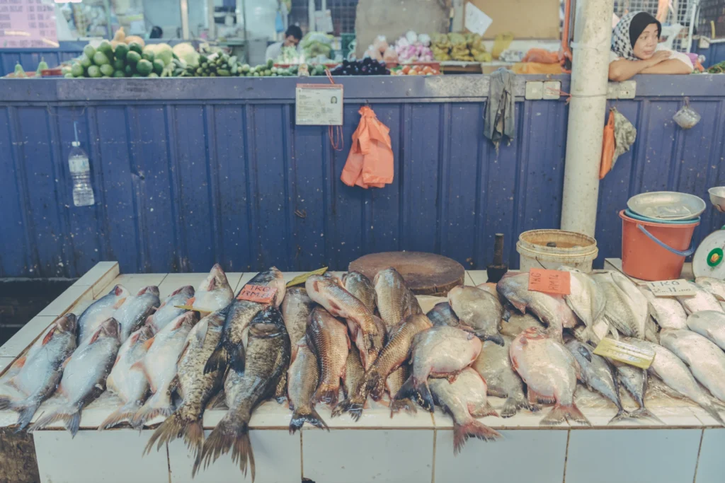 Rows of whole fish arranged on a tiled counter, with a market vendor standing behind the stall in Hong Kong.