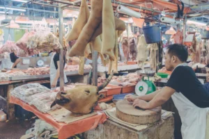 Butcher working at a chopping block beneath hanging poultry at a wet market in Malaysia.