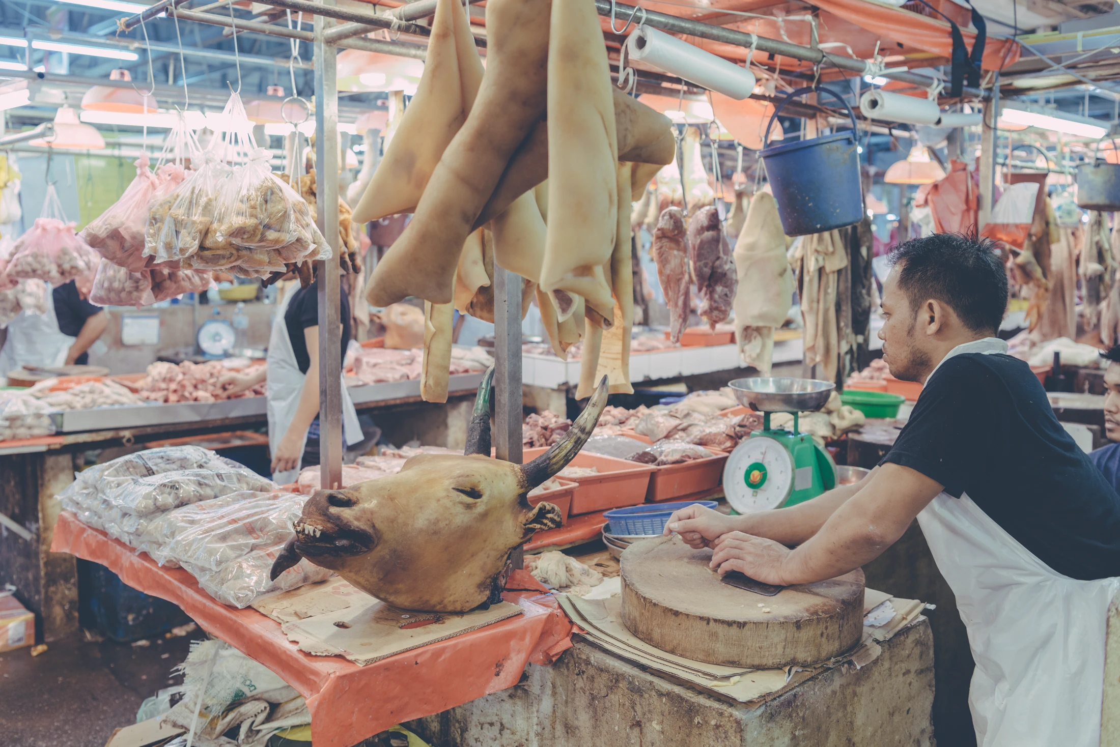 Butcher working at a chopping block beneath hanging poultry at a wet market in Malaysia.