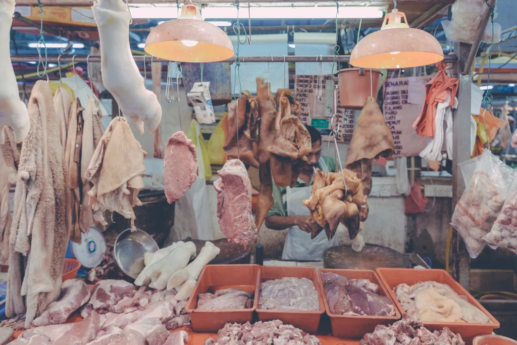 Malaysian butcher stall with hanging poultry, cuts of meat and trays arranged across the counter.