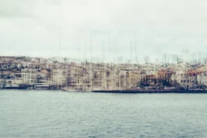 Pale multilayer photograph of Istanbul’s waterfront across the water, with overlapping historic buildings and the Galata Tower emerging through a hazy skyline.