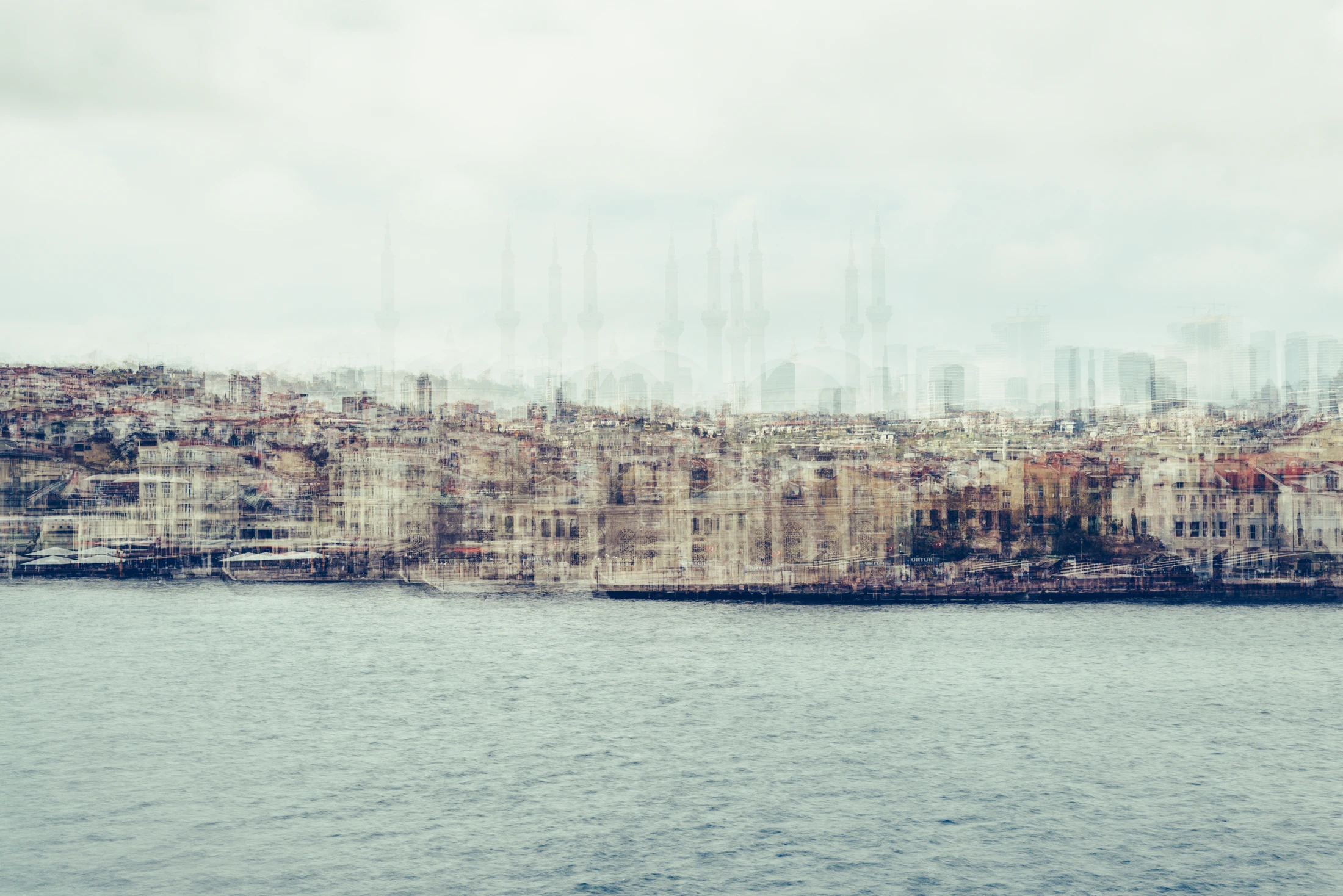 Pale multilayer photograph of Istanbul’s waterfront across the water, with overlapping historic buildings and the Galata Tower emerging through a hazy skyline.