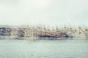 Pale multilayer photograph of Istanbul’s waterfront across the water, with overlapping historic buildings and the Galata Tower emerging through a hazy skyline.