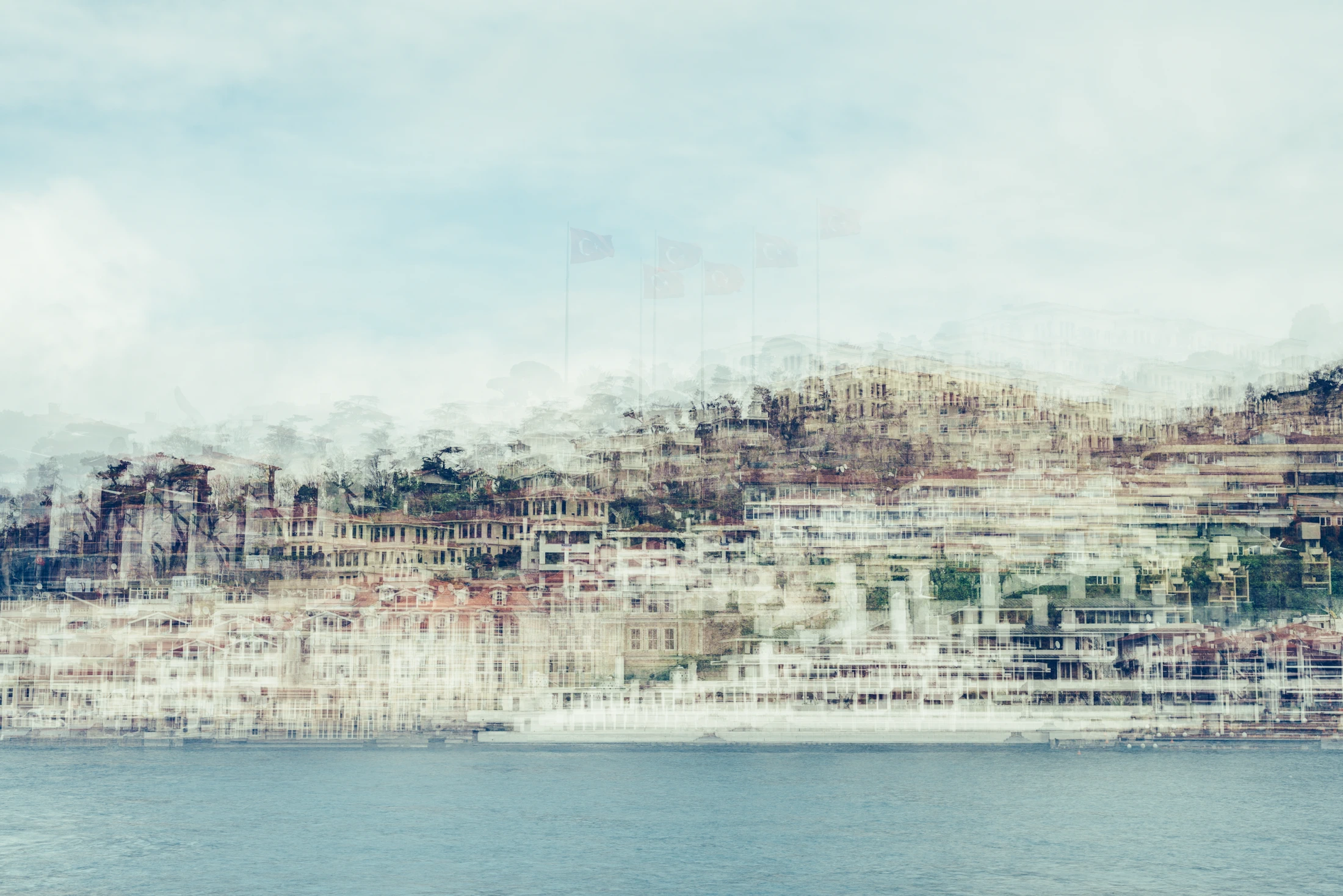 Pale multilayer photograph of Istanbul’s waterfront across the water, with overlapping historic buildings and the Galata Tower emerging through a hazy skyline.
