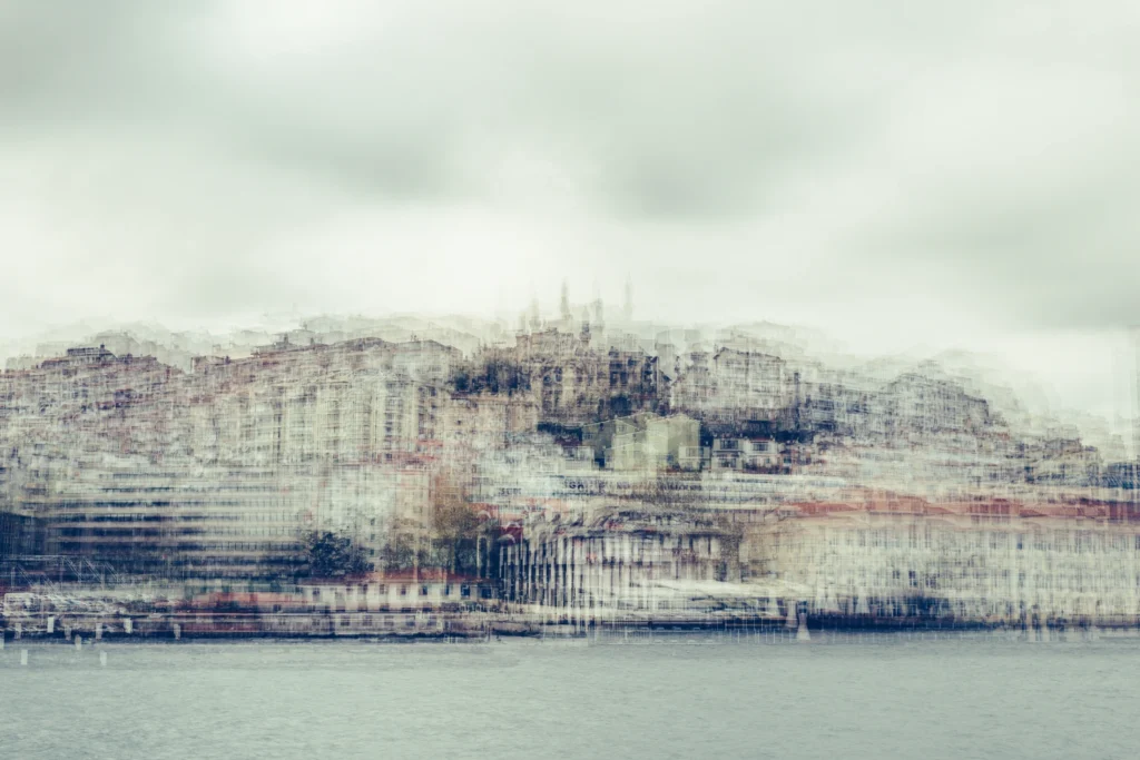 Pale multilayer photograph of Istanbul’s waterfront across the water, with overlapping historic buildings and the Galata Tower emerging through a hazy skyline.