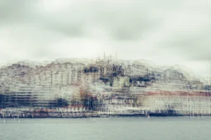 Pale multilayer photograph of Istanbul’s waterfront across the water, with overlapping historic buildings and the Galata Tower emerging through a hazy skyline.